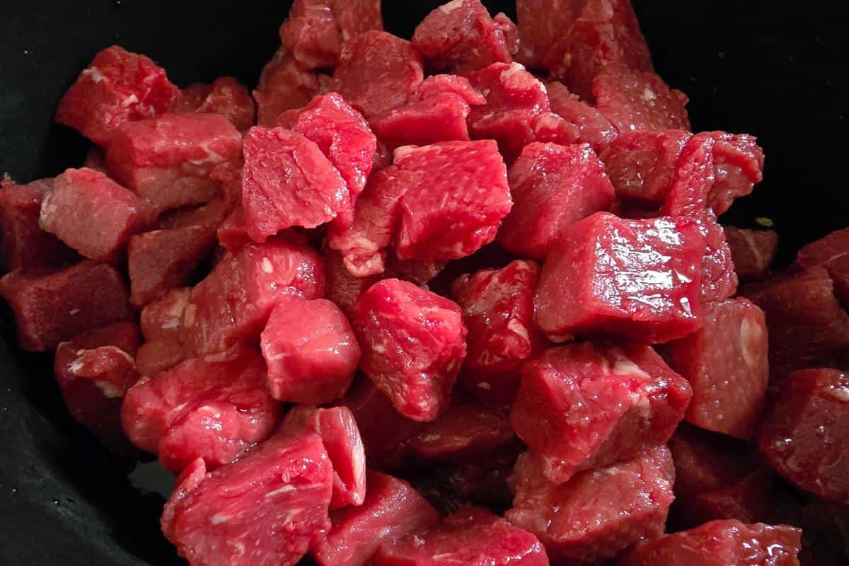 Chunks of raw red meat piled together in a close-up shot, ready to be transformed into a hearty root vegetable stew.