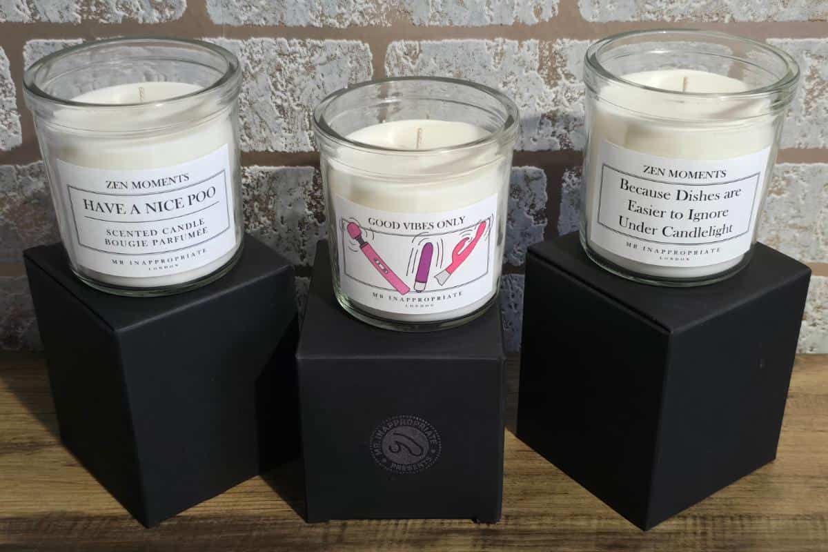 Discover three scented candles in glass jars perched on black boxes, each boasting humorous labels like "Have a Nice Poo" and "Good Vibes Only." Perfect for clients of Laugh and Blush or anyone exploring a Rude Gift Website.