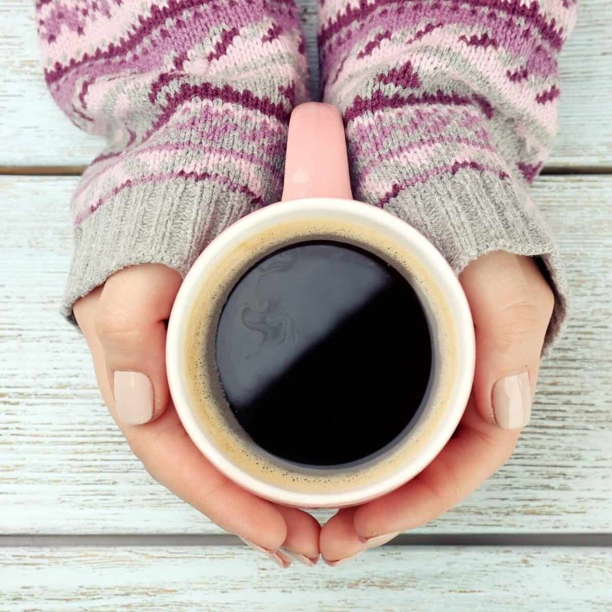Lady with cosy jumper holding a cup of coffee, only forearms showing