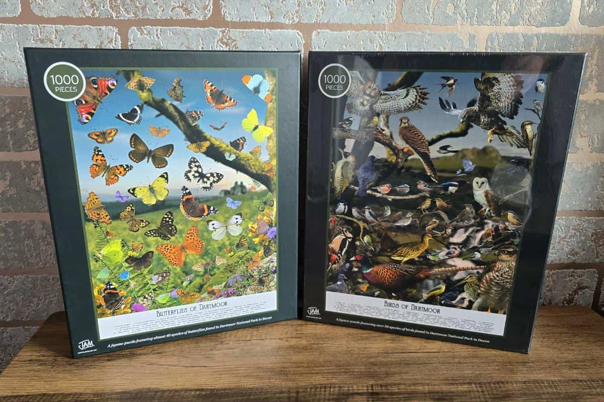 Two 1000-piece puzzles are elegantly displayed against a brick wall, perfect for a Mother’s Day gift. One features "Butterflies of Dartmoor" in a vibrant meadow, while the other showcases "Birds of Dartmoor" with diverse avian beauties—ideal additions to any Mum's collection.