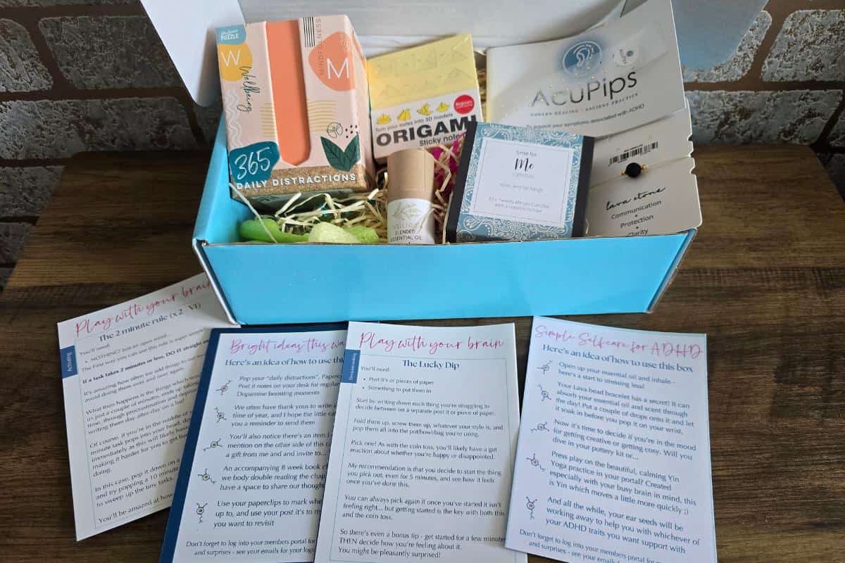 A subscription box is open on a table, perfect for a gift. Inside are thoughtful items like a journal, origami kit, candle, tea, and informational cards—a delightful gift guide for showing appreciation to your mum.