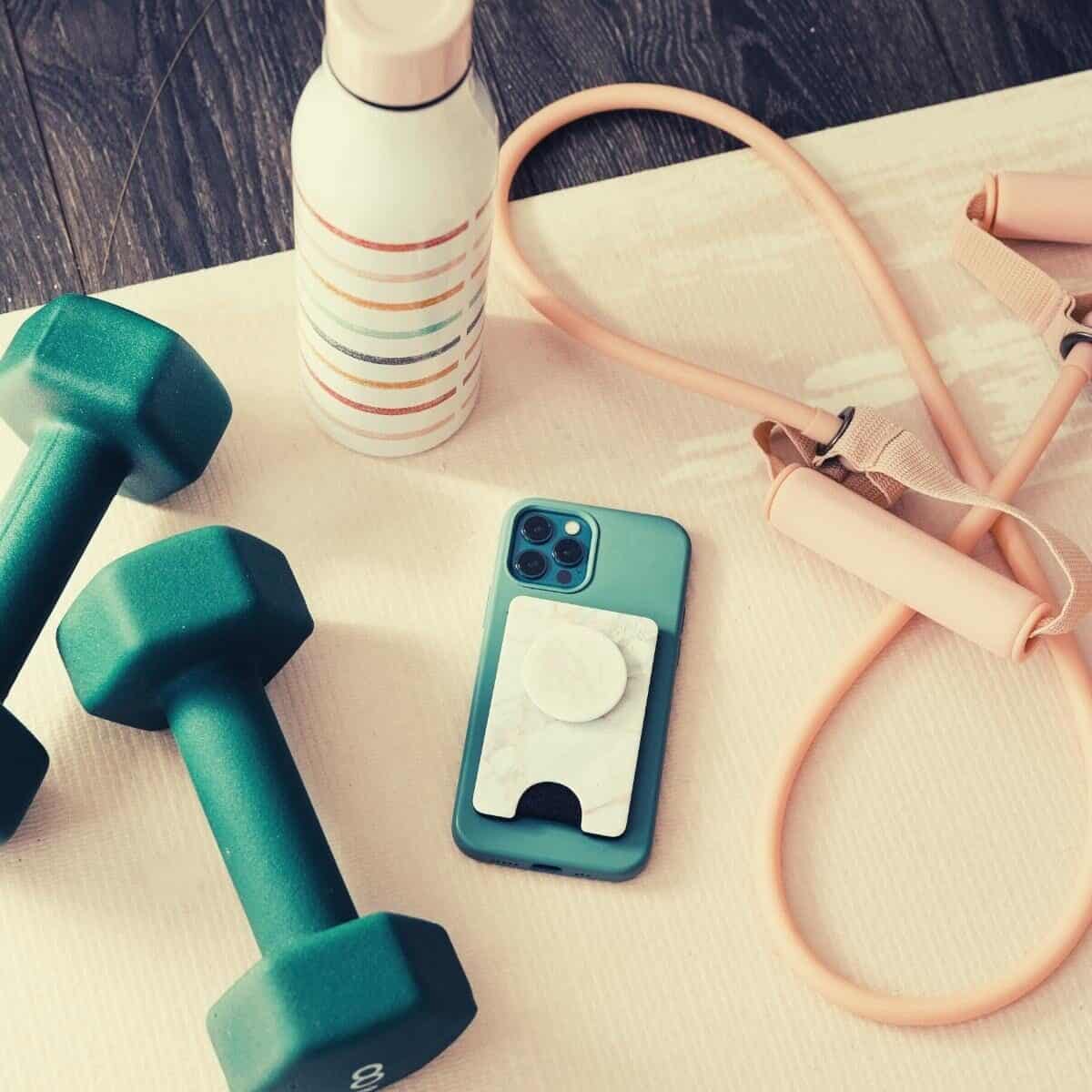 A selection of exercise gear on a table - small dumbbells, a skipping rope, a drink bottle and a mobile phone.