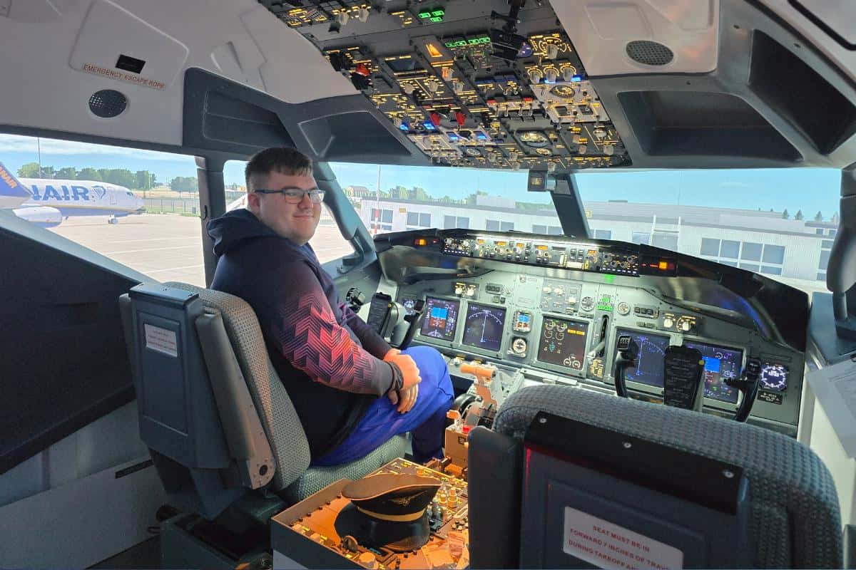 A person seated in a Flight Simulator cockpit at the FlightSimCentre, wearing a black and red long-sleeve shirt. The cockpit is filled with various controls and displays, capturing every detail of the immersive experience. An airplane with the word "Ryanair" is visible outside the window.