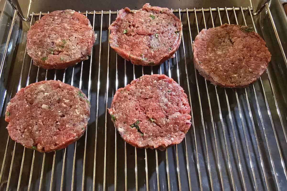 Five minted lamb burger patties rest on a metal grill rack, ready for easy cooking.