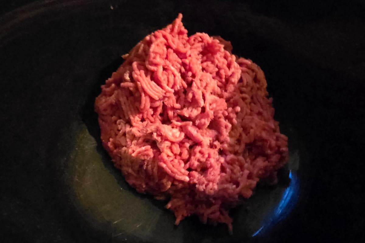A pile of raw ground beef rests on a dark surface, reminiscent of the ingredients for an easy recipe like a minted lamb burger.
