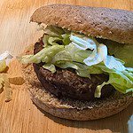 A minted lamb burger with a whole wheat bun, lettuce, and a beef patty rests on a wooden surface. Nearby, a few shreds of lettuce add to the healthy allure.