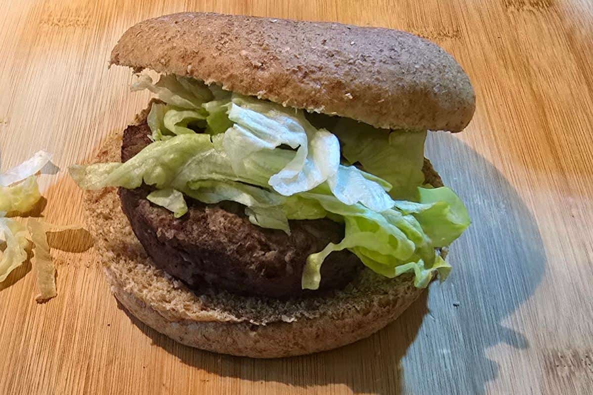 A minted lamb burger with a whole wheat bun, lettuce, and a beef patty rests on a wooden surface. Nearby, a few shreds of lettuce add to the healthy allure.