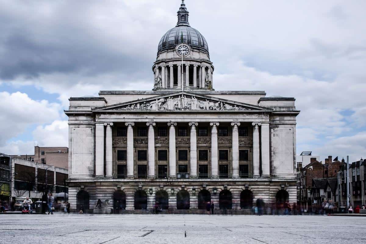 Set against a cloudy sky, this historic building in Nottinghamshire showcases grand columns and a majestic dome. People at the base provide a sense of scale and bustling activity, proving that exploring architectural wonders doesn't have to break the budget.