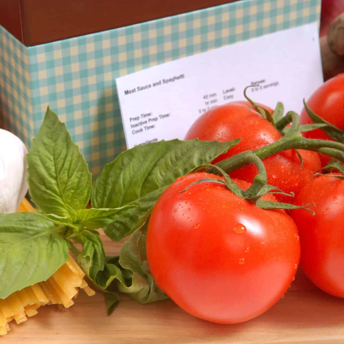 close up of a recipe box showing tomatoes and a recipe card in front of a checkered cardboard box